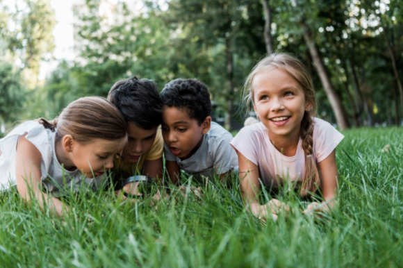 Children playing on some grass holding a magnifying glass