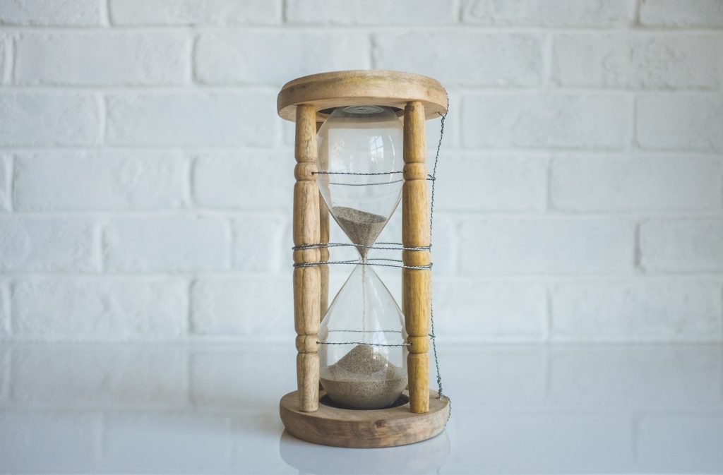 Clear hourglass with brown frame in front of a white brick wall